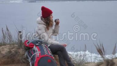 早春，一位戴着红帽子的迷人年轻女子背着一个大旅游背包，在森林里散步，喝酒